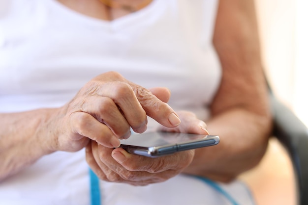 Closeup da velha avó segurando o celular moderno nas mãos mulher usando smartphone