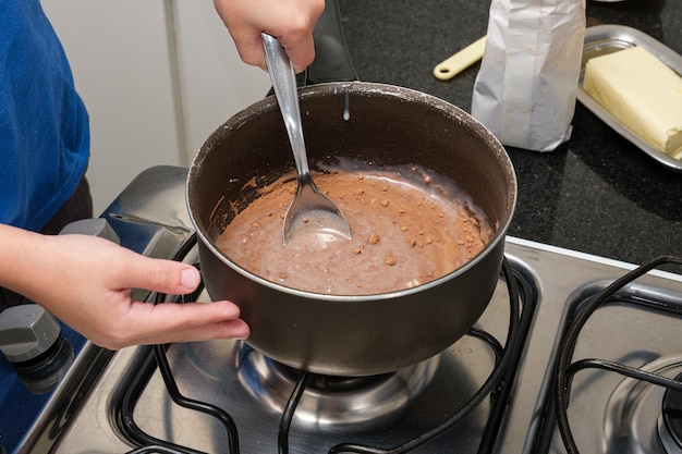 Closeup das mãos da criança mexendo com uma colher para fazer brigadeiro doce brasileiro