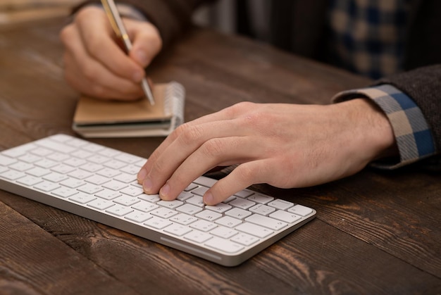 Closeup das mãos da pessoa anotando em papel branco digitando no teclado do computador