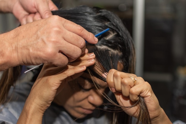 Closeup das mãos de um cabeleireiro profissional preparando o cabelo de uma mulher para tingir Foco seletivo