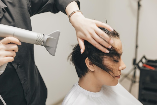 Closeup das mãos de um cabeleireiro secando o cabelo das mulheres com um corte de cabelo curto e estilo de secador de cabelo