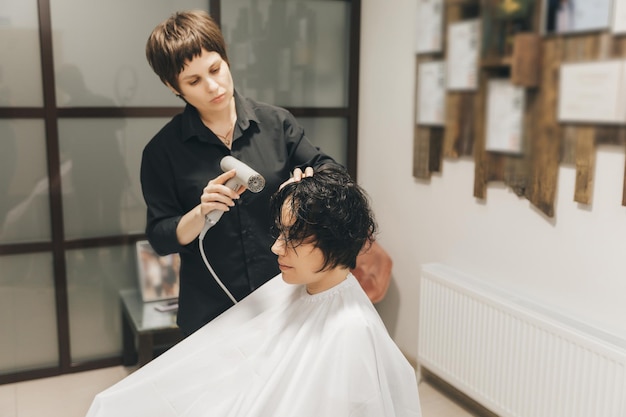 Closeup das mãos de um cabeleireiro secando o cabelo das mulheres com um corte de cabelo curto e estilo de secador de cabelo