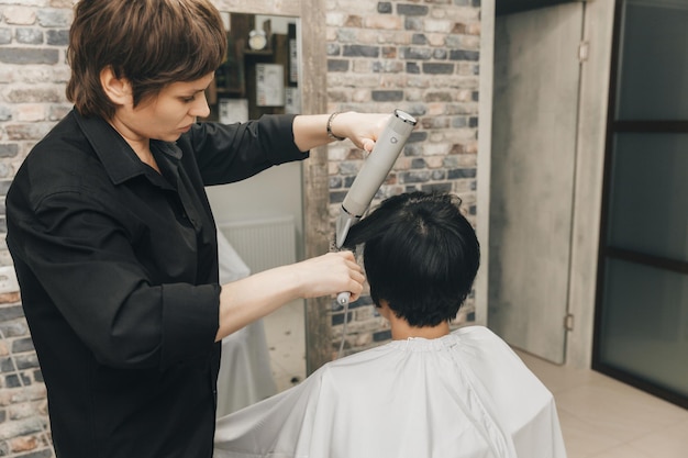 Closeup das mãos de um cabeleireiro secando o cabelo das mulheres com um corte de cabelo curto e estilo de secador de cabelo