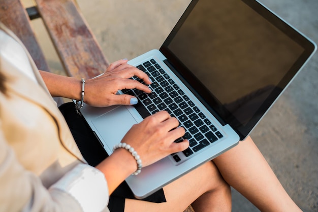 Closeup das mãos de uma executiva feminina trabalhando em seu laptop sentado em um banco em qualquer lugar ao ar livre