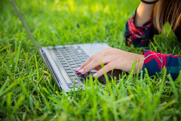 Closeup das mãos de uma garota digitando com laptop descansando em um campo de tecnologia ao ar livre