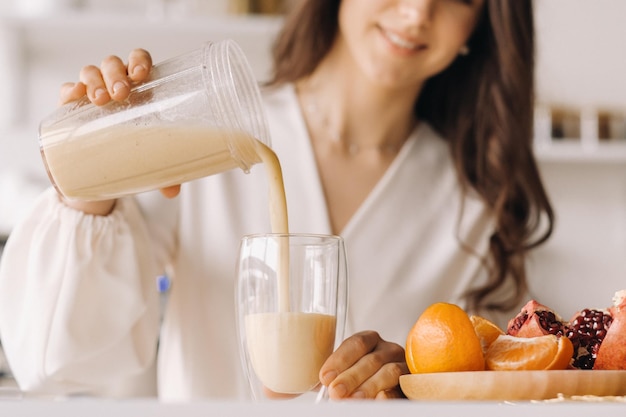 Closeup das mãos de uma menina derramando um coquetel de frutas frescas de bananas e uma laranja na cozinha Dieta para perda de peso