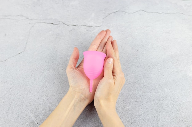 Closeup das mãos de uma mulher segurando um copo menstrual de silicone produto ecológico alternativo de higiene feminina durante a menstruação conceito sem desperdício