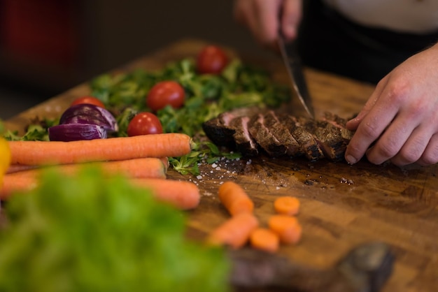 closeup das mãos do Chef na cozinha do hotel ou restaurante preparando bife com decoração de vegetais