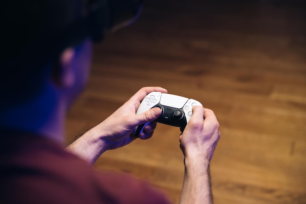 Closeup das mãos do homem jogando videogame no console de jogos na frente da TV widescreen Homem joga com Play station 5 Dual Sense controller Luzes coloridas