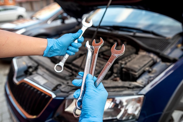 Closeup das mãos do mecânico de automóveis usando chave para reparar o motor do carro na garagem de automóveis