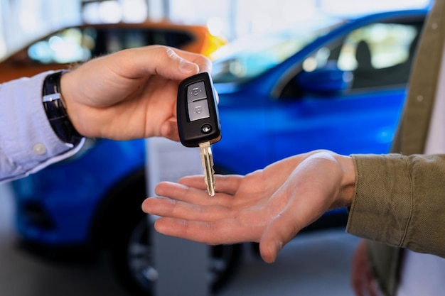 Closeup das mãos do vendedor que está entregando a chave do carro ao comprador no contexto dos carros no showroom