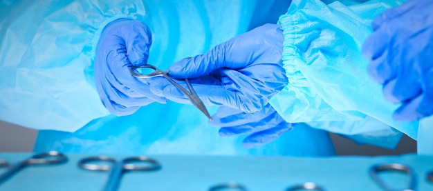 Closeup das mãos dos cirurgiões no trabalho na sala de cirurgia em tons de azul