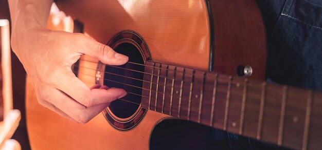 Closeup das mãos e dedos de um músico masculino tocando uma guitarra acústica Guitarra musical