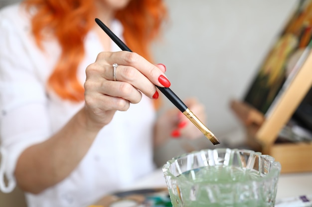 Closeup de artista feminina colocando pincel em um copo com água