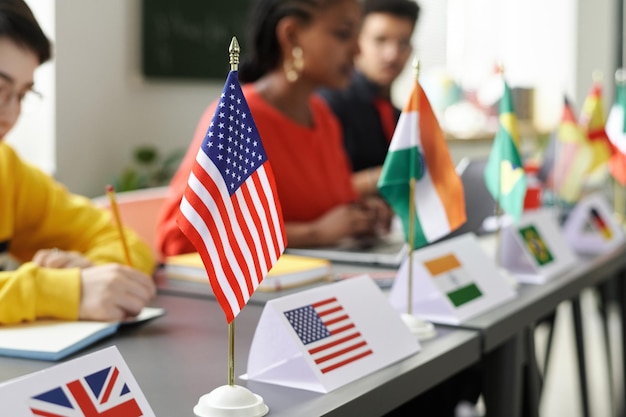 Closeup de bandeiras de diferentes países em cima da mesa com estudantes multirraciais estudando em segundo plano