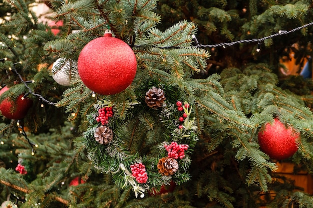 Closeup de bolas vermelhas de ano novo e guirlanda em um galho de árvore de Natal ao ar livre em dia de verão