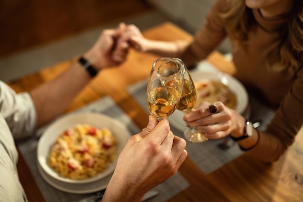 Closeup de casal irreconhecível brindando com champanhe enquanto de mãos dadas na mesa de jantar