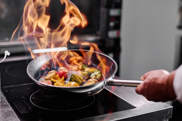 Closeup de chef profissional em uma cozinha comercial, cozinhando estilo flambe