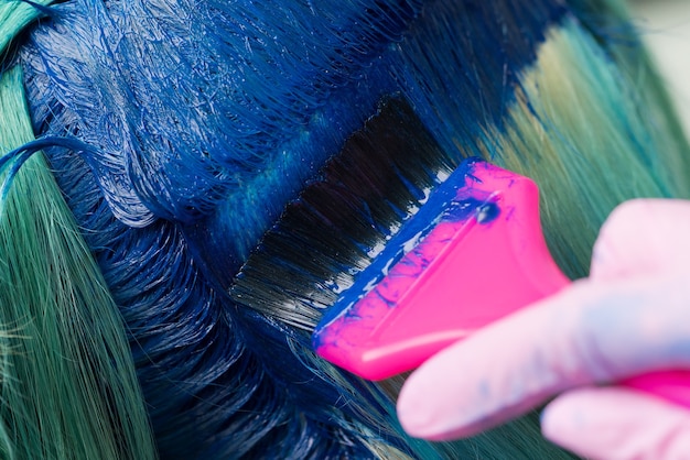 closeup de coloração de cabelo em cabeleireiro de salão de beleza usando uma escova rosa enquanto aplica tinta azul