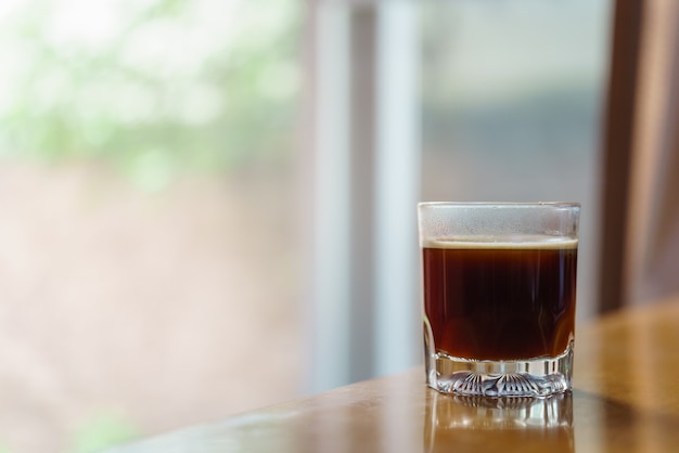 Closeup de copo de café preto quente Americano com sunlingt e sombra na mesa de madeira com espaço de cópia.