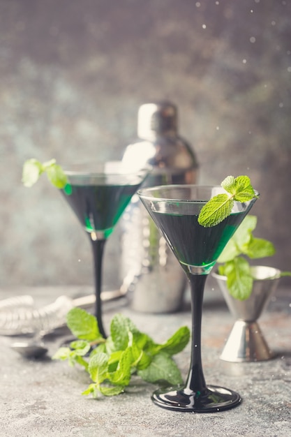 Closeup de coquetéis verdes em taças de martini com folhas de hortelã sobre cinza