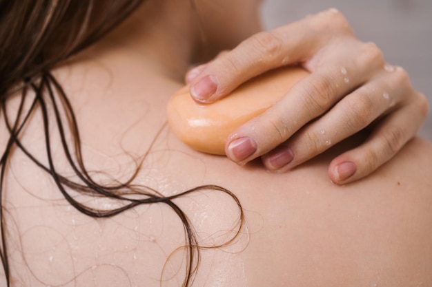 Foto closeup de costas femininas com a mão no ombro com uma barra de sabonete natural