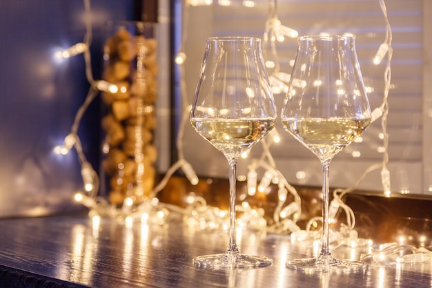 Closeup de dois copos de vinho branco em copos de cristal transparentes e guirlandas de luz