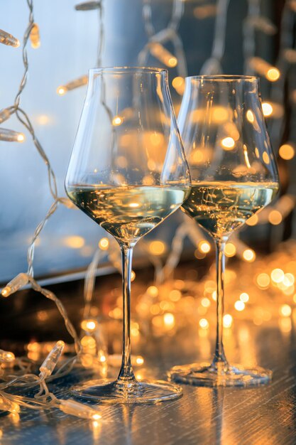 Closeup de dois copos de vinho branco em copos de cristal transparentes e guirlandas de luz