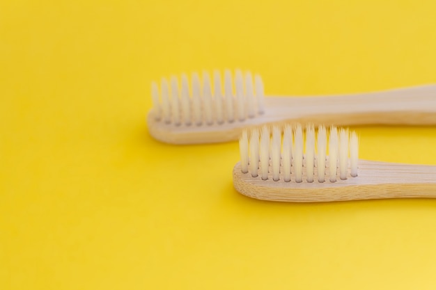 Closeup de duas escovas de dente naturais de madeira em fundo amarelo