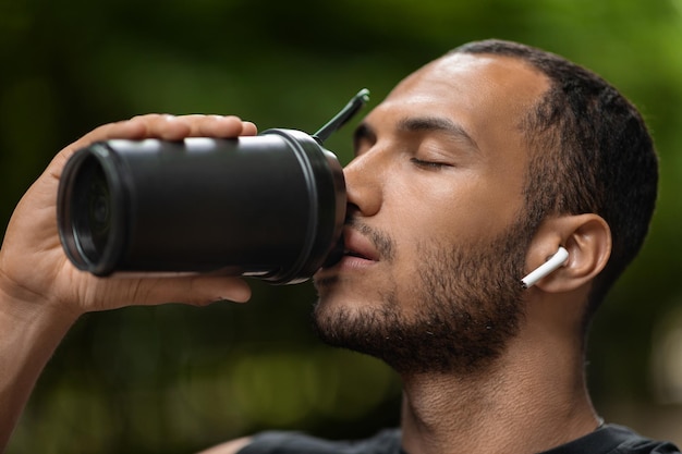 Closeup de esportista negro bonito bebendo treinamento de coquetel de proteína ao ar livre