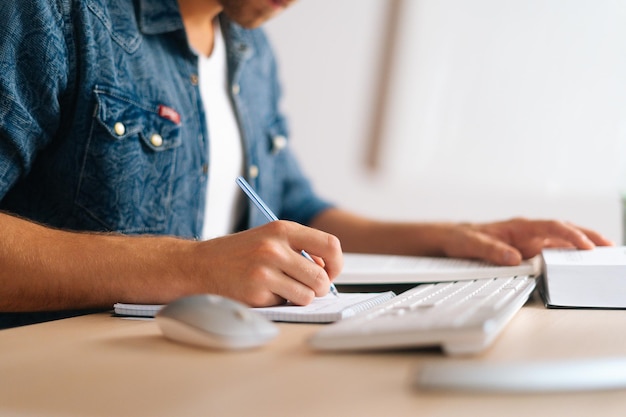 Foto closeup de estudante masculino irreconhecível estudando on-line em casa usando notas de escrita de computador assistindo aula de vídeo