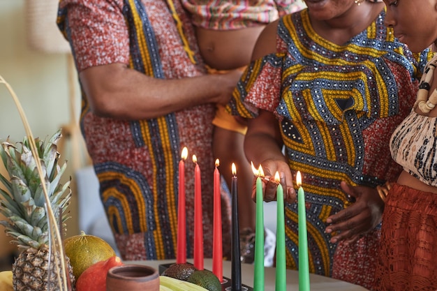 Closeup de família africana em trajes nacionais acendendo velas para celebrar o feriado de kwanzaa