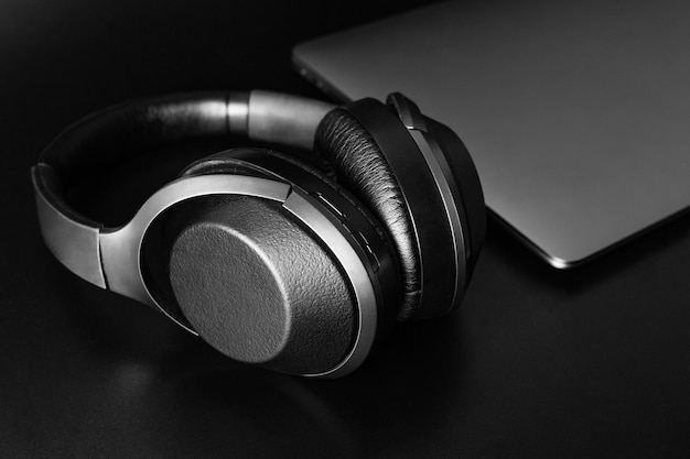 Closeup de fones de ouvido sem fio e laptop na mesa de fundo preto Música online