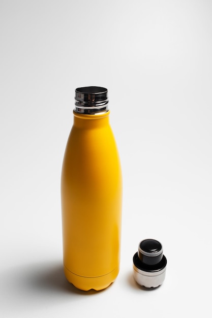 Closeup de garrafa de água reutilizável de aço de amarelo perto da tampa no fundo branco