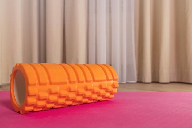 Closeup de grande rolo laranja para massagem miofascial em fundo rosa em casa