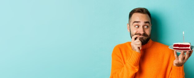 Closeup de homem adulto feliz comemorando aniversário segurando bolo de aniversário com vela e fazendo desejo standi