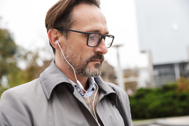 Closeup de imagem de empresário confiante usando óculos, usando fones de ouvido, enquanto caminha na rua da cidade