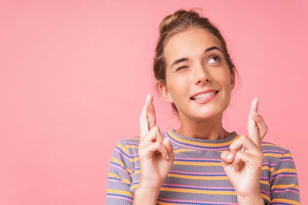 Closeup de imagem positiva de mulher bonita sorrindo e sonhando com os dedos cruzados isolados sobre a parede rosa