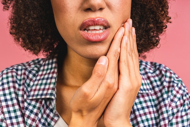 Foto closeup de jovem afro-americana sobre fundo rosa isolado tocando a boca com a mão com expressão dolorosa por causa de dor de dente ou doença dentária nos dentes conceito de dentista