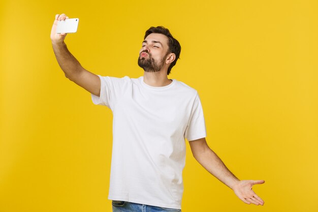 Closeup de jovem bonito olhando para smartphone e tomar selfie. isolar sobre amarelo.