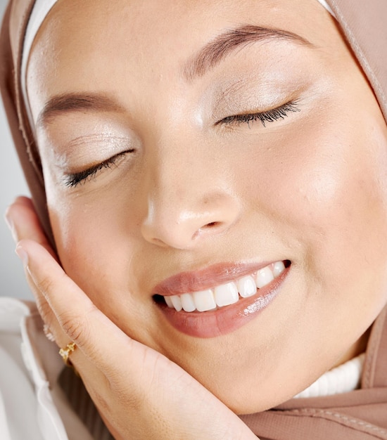 Foto closeup de linda mulher muçulmana com os olhos fechados sentindo-se satisfeita com sua rotina de cuidados com a pele tiro na cabeça de uma senhora deslumbrante com maquiagem brilhante e lenço marrom tocando seu rosto modéstia e beleza