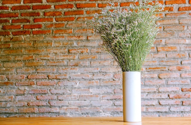 Closeup de lindas flores em um vaso de cerâmica branco sobre mesa de madeira e fundo de parede de tijolos embaçados