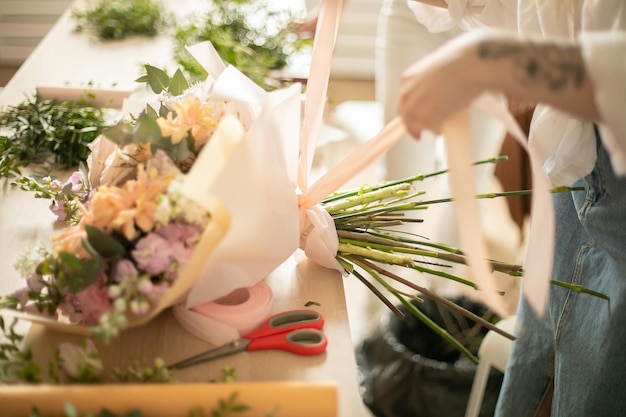 Closeup de mãos de florista jovem fazendo buquê de flores com fita