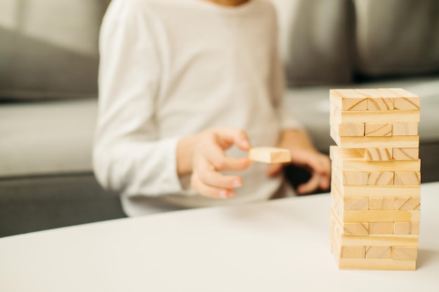 Closeup de mãos de meninos em uma camiseta branca brinca em casa na mesa em Jenga Jogos de tabuleiro para crianças