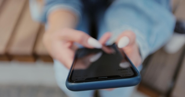 Closeup de mãos de mulher com mensageiro de mensagens de texto para smartphone no banco da rua Mulher usando aplicativo de mídia social no smartphone