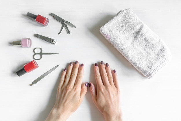 Closeup de mãos de mulher com unhas polidas e instrumentos de manicure, frascos de esmalte. mulher caucasiana, recebendo manicure francesa em casa ou no salão de beleza. autocuidado, procedimentos de beleza você mesmo.