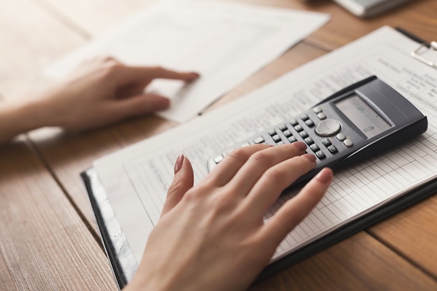 Closeup de mãos de mulher, contando com calculadora e lendo documentos. Antecedentes financeiros, contar e pagar uma conta, espaço de cópia