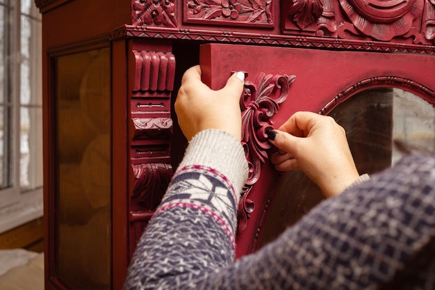 Closeup de mãos de mulheres de meia-idade colando novos ornamentos de madeira esculpidos em papelão vermelho na oficina para restauração de móveis Reutilização ecológica de coisas velhas