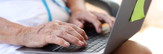 Closeup de mãos de velha digitando no laptop moderno, mulher idosa digitando no laptop de trabalho remoto