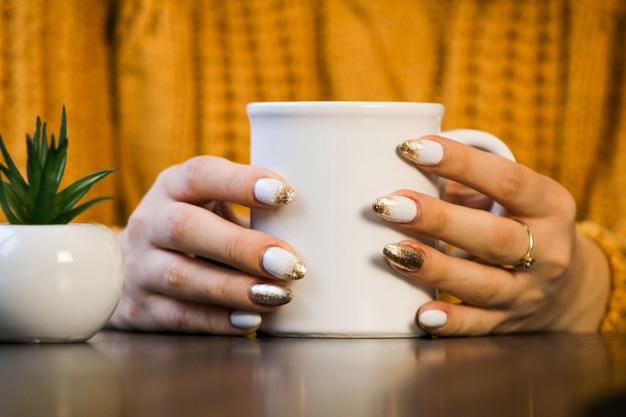 closeup de mãos femininas com uma caneca de bebida. Mulher bonita em suéter amarelo segurando uma xícara de chá